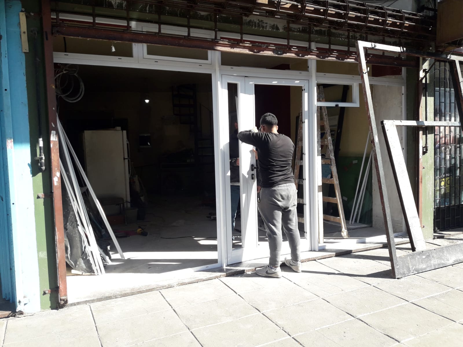 Frente de local comercial en Liniers con cerramiento de aluminio blanco línea Módena: puerta de dos hojas, paños y banderolas