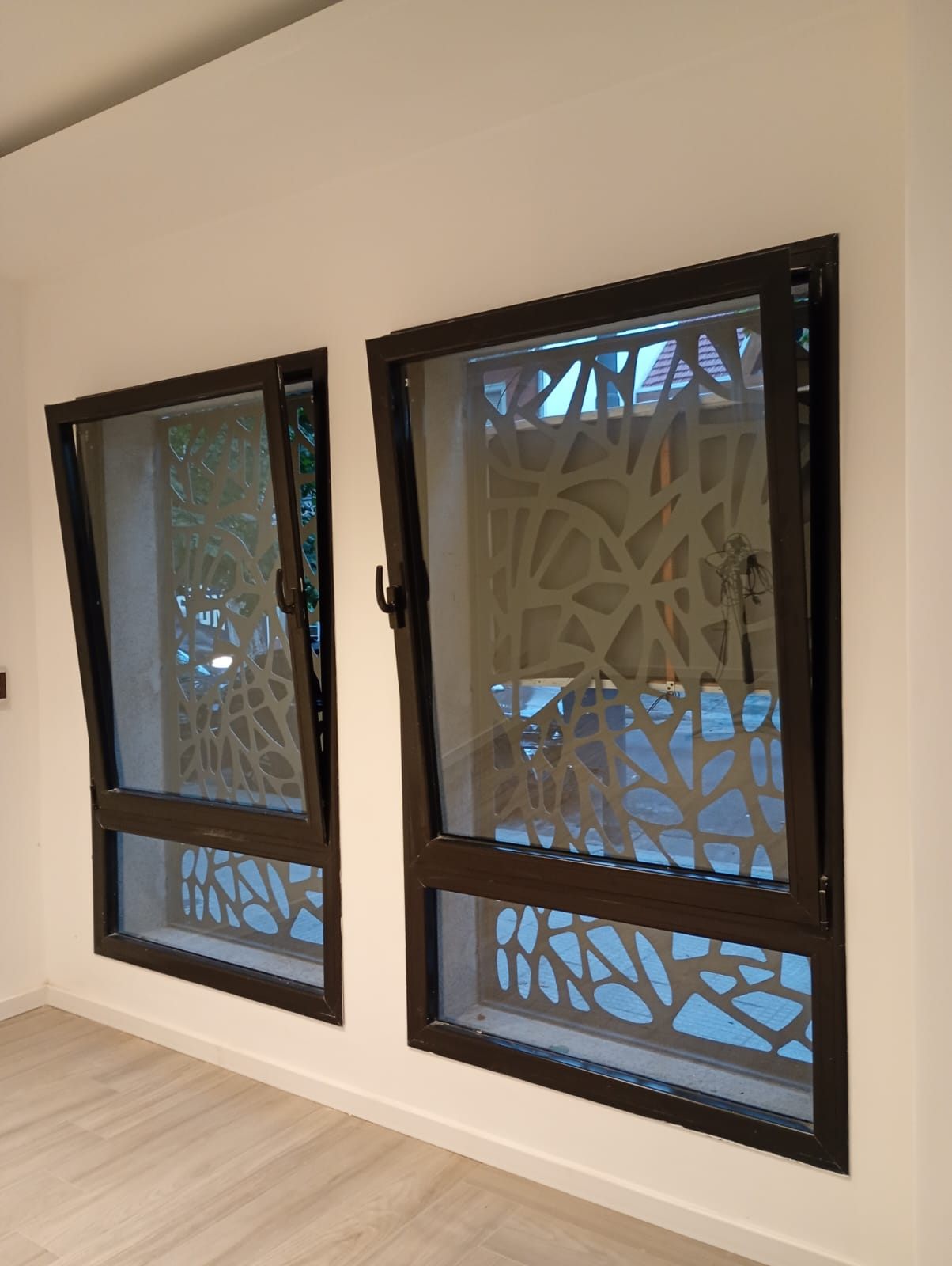 Dos ventanas oscilobatientes negras inclinadas para ventilar, frente a un panel calado