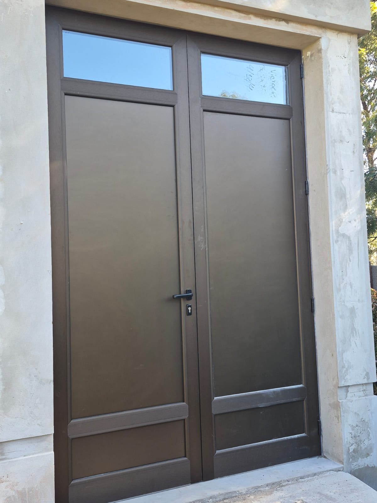 Puerta doble de aluminio color bronce con banderolas de vidrio