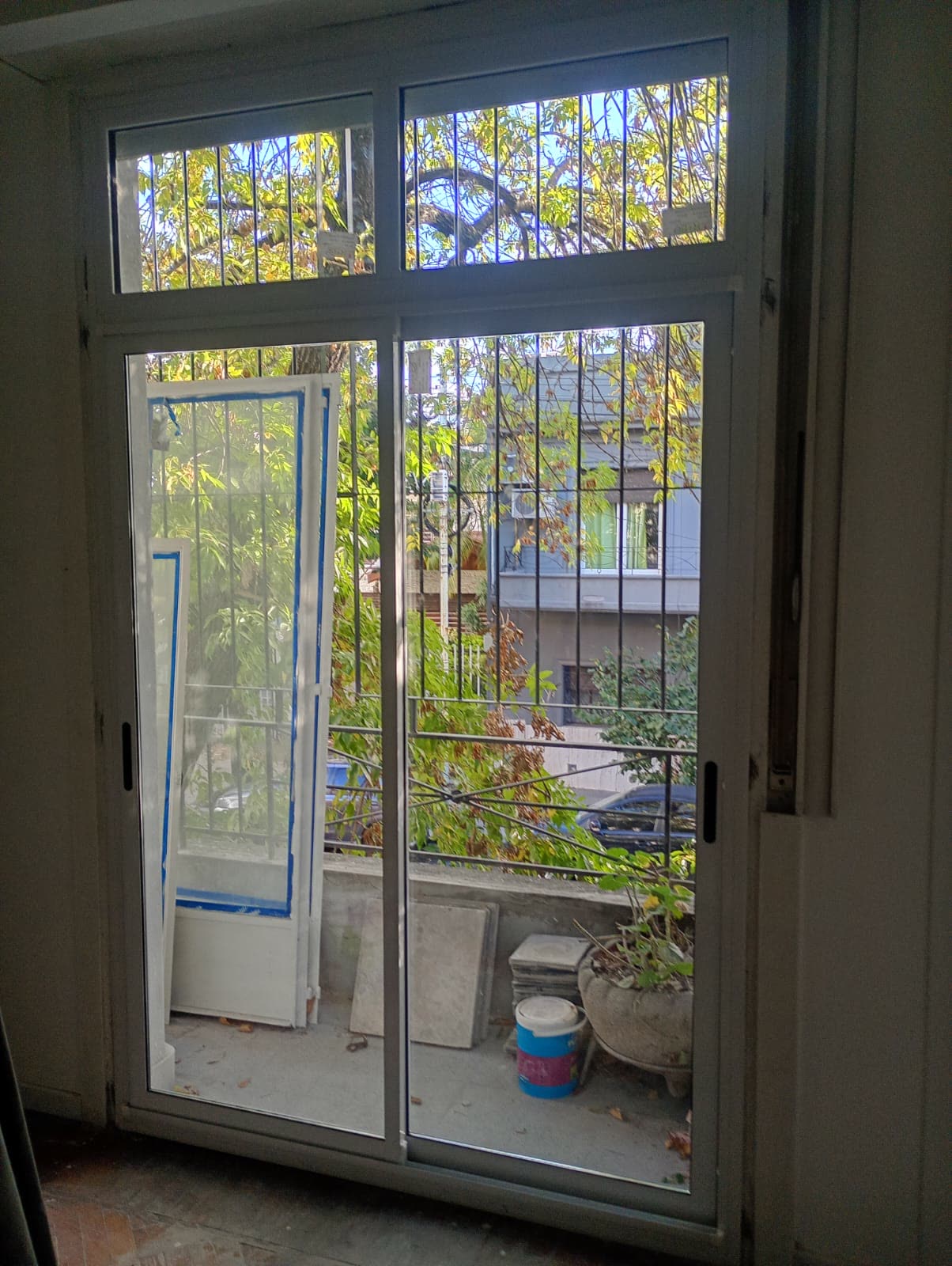 Puerta ventana blanca con banderola hacia un balcón con plantas