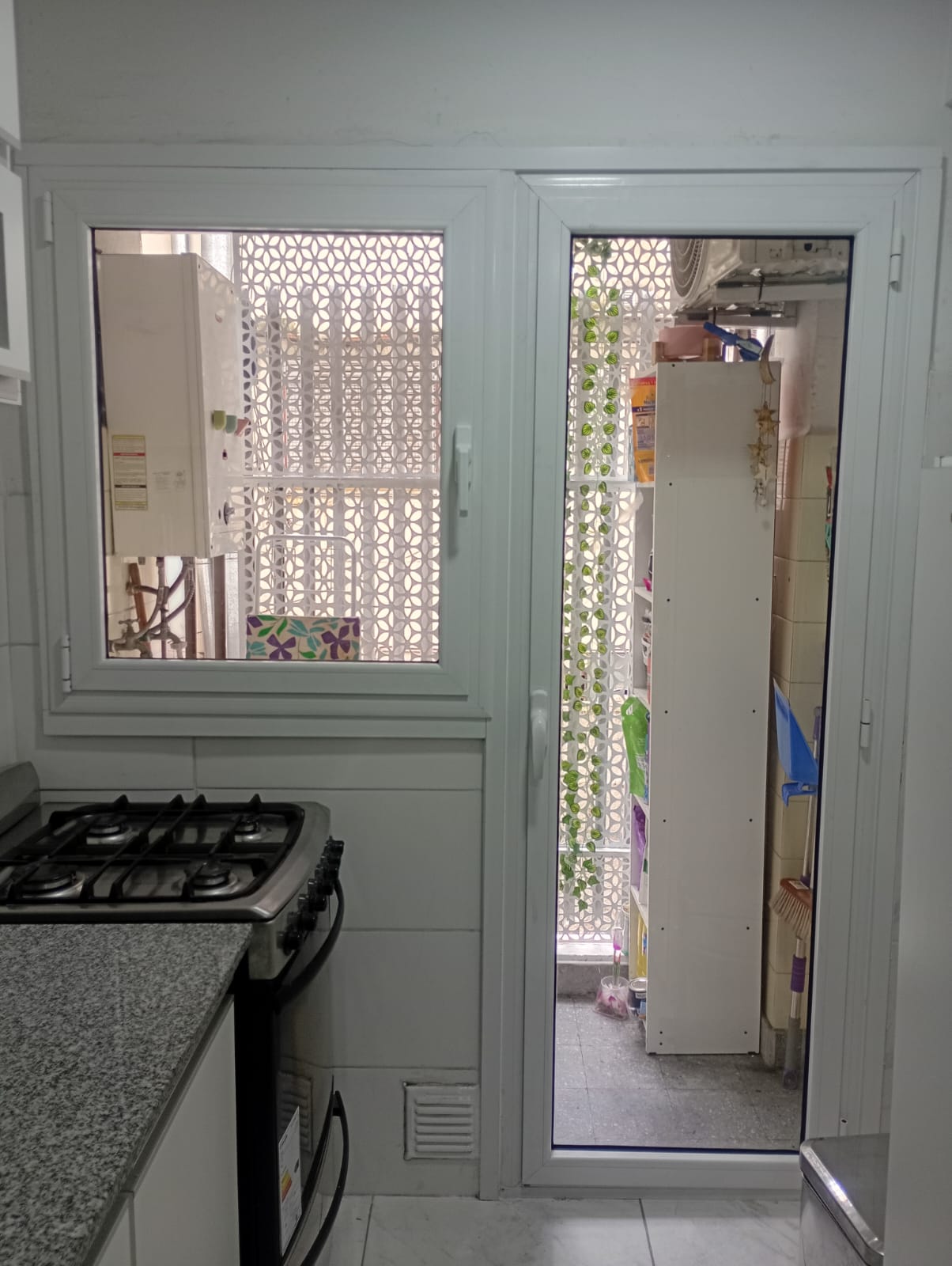 Cocina con puerta rebatible y ventana oscilobatiente blancas hacia el lavadero